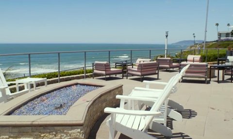 Eine Terrasse mit weißen Liegestühlen und einem Feuerplatz, der einen atemberaubenden Blick auf den Ozean bietet.