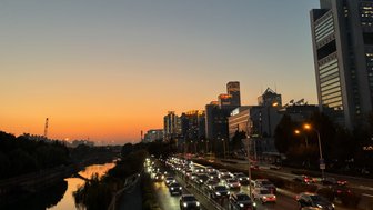 Ein malerischer Sonnenuntergang über einer Stadt, mit reflektierendem Wasser und beleuchteten Gebäuden im Hintergrund.