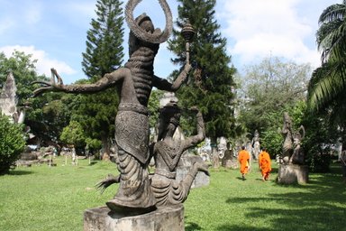 Im Buddha-Park in Vientiane stehen beeindruckende Statuen, während Mönche in orangefarbener Robe vorbeigehen.