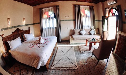 Ein elegantes Zimmer mit einem großen Bett, dekoriert mit Rosenblättern, und einem gemütlichen Sitzbereich.