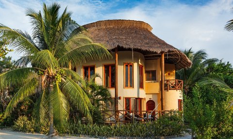 Ein charmantes Hotel mit einem strohgedeckten Dach, umgeben von üppigen Palmen und tropischer Vegetation.