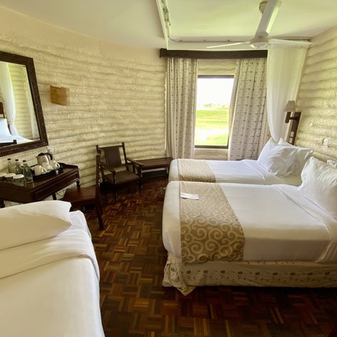 Ein gemütliches Zimmer mit zwei Einzelbetten, einem großen Spiegel und einem Fenster, das auf eine grüne Wiese blickt.