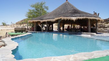 Ein einladender Pool in der Wüste, umgeben von einem strohgedeckten Pavillon und karger Landschaft.