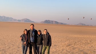 Eine Familie steht in der Wüste und im Hintergrund fliegen Heißluftballons - Namibia Familienurlaub