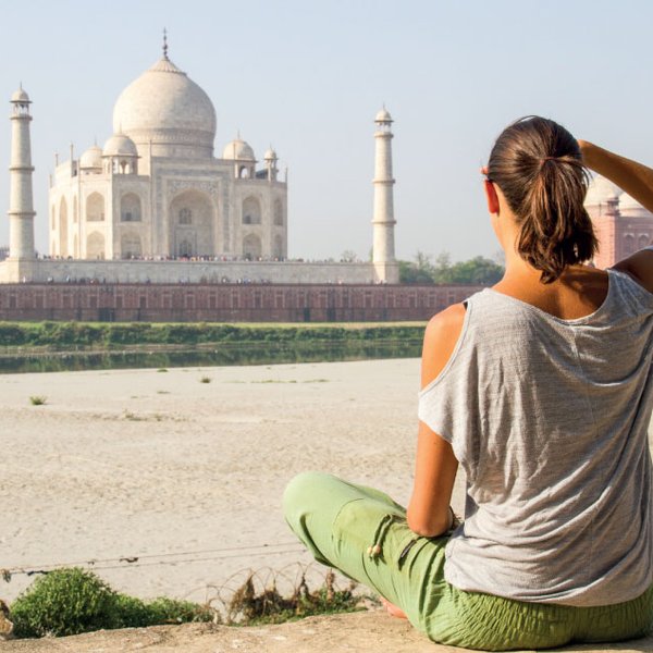 Eine Person sitzt am Ufer und betrachtet das majestätische Taj Mahal, umgeben von einer ruhigen Landschaft.