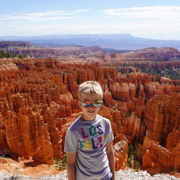 Ein Junge mit Sonnenbrille steht vor den beeindruckenden, orangefarbenen Felsformationen des Bryce Canyon Nationalparks.