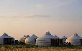 In der sanften Abenddämmerung stehen mehrere Jurten in einer weiten Graslandschaft, umgeben von sanften Hügeln.