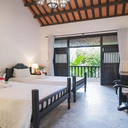 Ein helles Zimmer mit zwei Einzelbetten, eleganten Möbeln und Blick auf einen grünen Garten durch große Fenster.