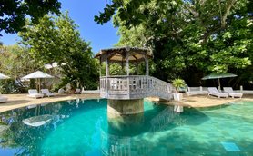 Ein ruhiger Poolbereich mit klarem Wasser, umgeben von üppigem Grün und einem charmanten Pavillon im Hintergrund.