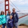 Eine Familie posiert fröhlich vor der Golden Gate Bridge, umgeben von einer malerischen Küstenlandschaft und sanften Wolken.