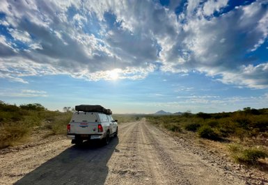 Ein Auto mit Dachzelt fährt auf einer einsamen Straße - Namibia Urlaub mit Kindern