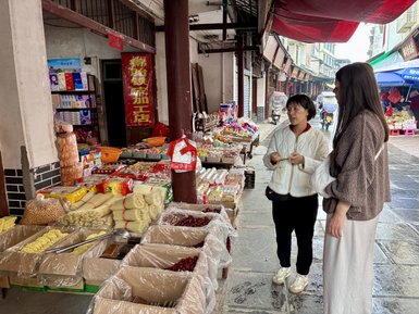 Zwei Frauen stehen in einem lebhaften Markt, umgeben von bunten Ständen mit Lebensmitteln und Snacks.