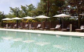 Ein ruhiger Poolbereich mit glitzerndem Wasser, umgeben von Liegen und Sonnenschirmen unter blauem Himmel.