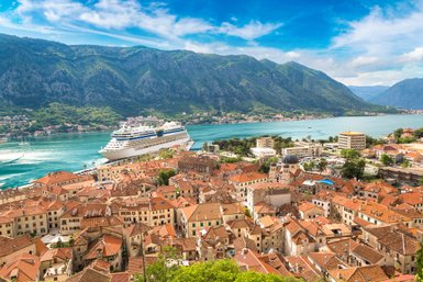 Eine atemberaubende Panoramaansicht von Kotor mit einem großen Kreuzfahrtschiff im Hafen und den majestätischen Bergen im Hintergrund.