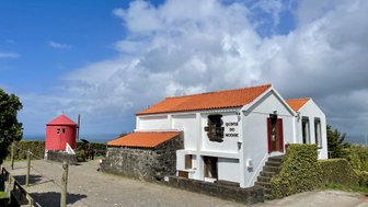 Ein charmantes, weißes Gebäude mit rotem Dach und Fensterläden, umgeben von üppigem Grün und einem blauen Himmel.