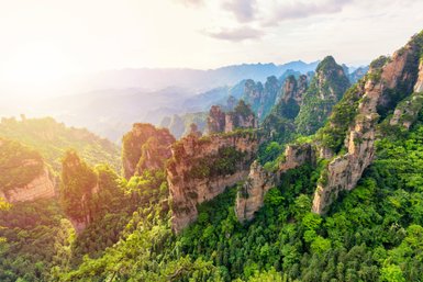 Eine atemberaubende Aussicht auf grüne Berge, die in der Morgensonne leuchten, mit schroffen Felsen und üppiger Vegetation.