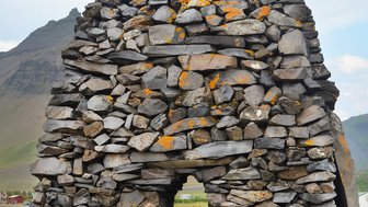 Zwei Kinder stehen vor einem beeindruckenden Steindenkmal, das mit Moos und Flechten bedeckt ist, in einer malerischen Landschaft.