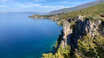 Ein atemberaubender Blick auf den Ohridsee, umgeben von sanften Hügeln und klarem, blauem Wasser unter einem strahlend blauen Himmel.