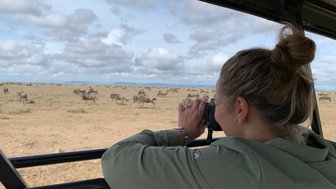 Frau beobachtet aufmerksam die Tierwelt mit Fernglas – Tansania mit Kindern