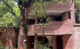 Ein modernes Gebäude mit rotem Ziegelstein, umgeben von üppigem Grün und großen Bäumen, strahlt eine einladende Atmosphäre aus.