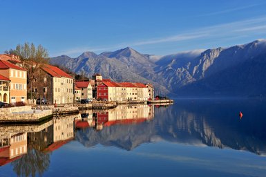 Die ruhige Bucht von Boka zeigt malerische Häuser mit roten Dächern, die sich im glatten Wasser spiegeln.