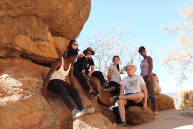 Eine Reisegruppe sitzt gemeinsam im Schatten eines Felsens an der Spitzkoppe - Namibia mit Kindern