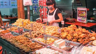Eine Verkäuferin in einem Streetfood-Markt bereitet eine Vielzahl von frittierten Snacks und Meeresfrüchten vor.