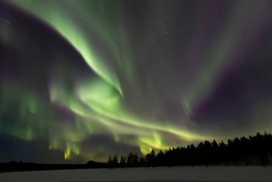 Die Nordlichter tanzen in lebhaften Grüntönen über den nächtlichen Himmel, während der Schnee sanft im Licht schimmert.