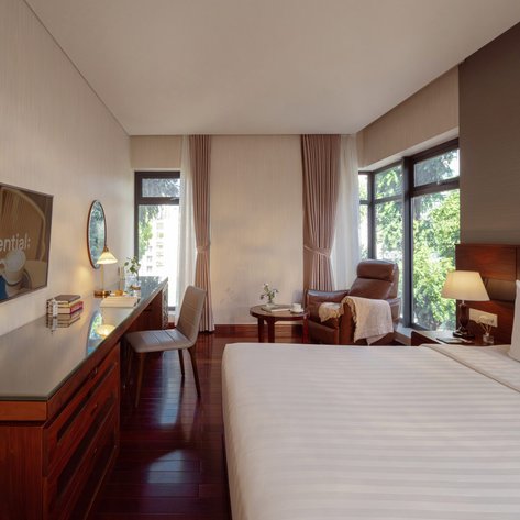 Ein elegantes Hotelzimmer mit einem großen Bett, einem Schreibtisch und einem gemütlichen Sessel neben einem Fenster.