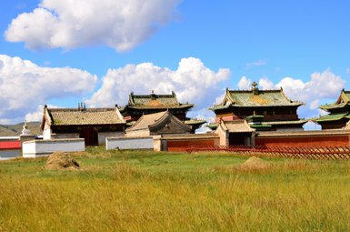 Die beeindruckenden Tempel von Erdene Zuu in der mongolischen Steppe, umgeben von üppigem Gras und strahlend blauem Himmel.