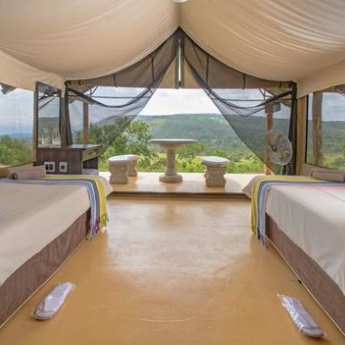 Ein geräumiges Zeltzimmer mit zwei Betten, das einen atemberaubenden Blick auf die grüne Landschaft bietet.