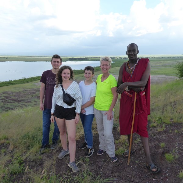 Eine Gruppe von fünf Personen steht auf einem Hügel mit Blick auf eine grüne Landschaft und einen ruhigen See im Hintergrund.