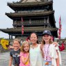 Vier Mädchen stehen fröhlich vor einem historischen Torturm in Xi'an und lächeln in die Kamera, während bunte Laternen im Hintergrund schweben.