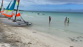Am Strand von Cayo Santa Maria stehen Segelboote mit bunten Segeln, während Familien im flachen Wasser spielen.