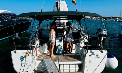 Zwei Frauen stehen auf einem Segelboot, das an einem Steg im Hafen festgemacht ist, umgeben von anderen Yachten.