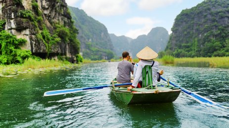 Zwei Personen sitzen in einem Boot und genießen die ruhige Landschaft mit hohen, bewaldeten Klippen im Hintergrund.
