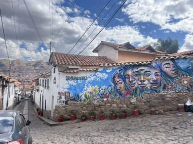 Bunte Wandmalerei mit Gesichtern und Blumen an einem weißen Gebäude in einer steilen Straße in Cusco.