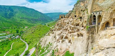 Die beeindruckenden Höhlenwohnungen sind in die steilen Felsen einer grünen Landschaft eingebaut, umgeben von Bergen.