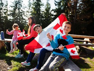 Eine Gruppe von Kindern sitzt im Freien und hält kanadische Flaggen, während sie fröhlich in die Kamera lächeln.