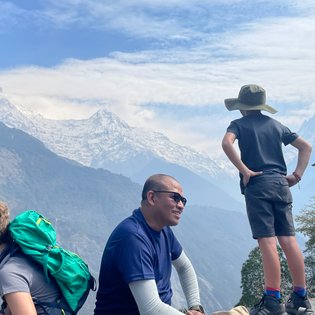 Ein Junge mit einem Hut steht nachdenklich auf einem Felsen und blickt auf die majestätischen schneebedeckten Berge.