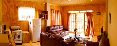 Ein gemütlicher Wohnraum mit braunen Ledermöbeln, einem Tisch und großen Fenstern, die viel Licht hereinlassen.