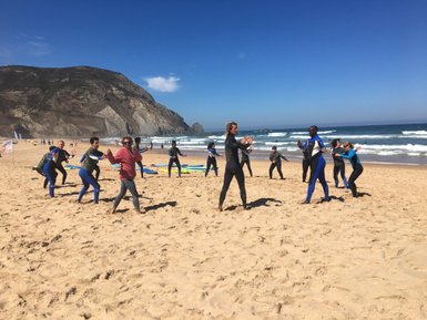 Eine Gruppe von Surfschülern übt auf dem Sandstrand, umgeben von Wellen und einer malerischen Küstenlandschaft.