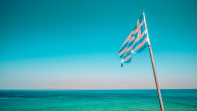 Eine griechische Flagge weht sanft über dem klaren, blauen Wasser des Meeres unter einem strahlend blauen Himmel.