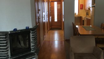 Ein gemütlicher Wohnraum mit einem Kamin aus Stein, Holzfußboden und einem großen Esstisch im Hintergrund.