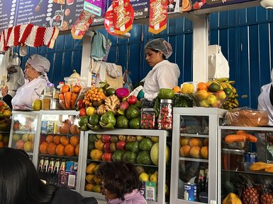 Ein lebhafter Marktstand in Cusco mit frischen Früchten und zwei Verkäuferinnen in weißen Schürzen, die Kunden bedienen.