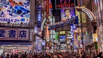 Bunte Neonlichter erhellen eine belebte Straße in Tokio, wo Menschen zwischen Geschäften und Werbetafeln schlendern.