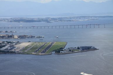 Ein Flugzeug startet über dem Wasser und dem Flughafen Santos Dumont, umgeben von einer malerischen Landschaft.