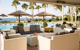 Ein eleganter Außenbereich mit weißen Sofas und einem Glastisch, umgeben von Palmen und einem Pool mit Meerblick.
