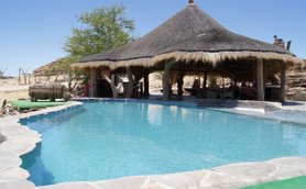 Ein einladender Pool in der Wüste, umgeben von einem strohgedeckten Pavillon und karger Landschaft.