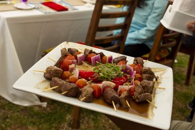 Ein Teller mit gegrilltem Fleisch und buntem Gemüse, kunstvoll auf Spießen angerichtet, wird von einer Hand gehalten.